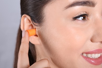 Photo of Young woman inserting foam ear plug on grey background, closeup