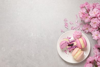 Delicious colorful macarons and pink flowers on grey table, flat lay. Space for text