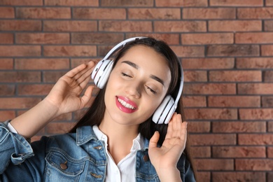 Photo of Beautiful young woman listening to music with headphones against brick wall