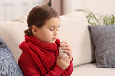 Photo of Cute little girl holding nasal spray on sofa at home