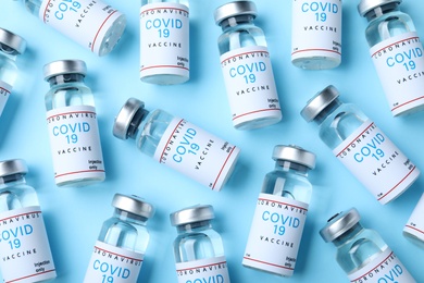 Photo of Glass vials with COVID-19 vaccine on light blue background, flat lay