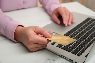 Online payment. Woman using credit card and laptop at white marble table indoors, closeup