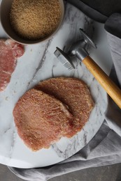 Cooking schnitzel. Raw pork chops in bread crumbs and meat mallet on grey table, top view