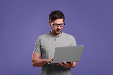 Handsome man with laptop on lilac background