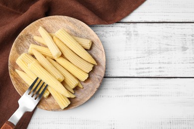Photo of Pickled baby corn and fork on white wooden table, top view. Space for text