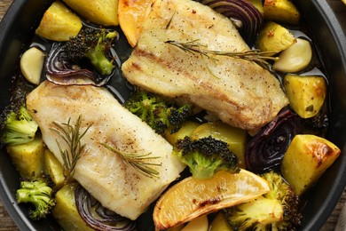 Photo of Pieces of delicious baked cod with vegetables, lemon and spices in dish, top view
