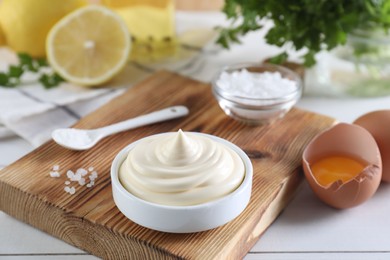 Photo of Fresh mayonnaise sauce in bowl and ingredients on white wooden table