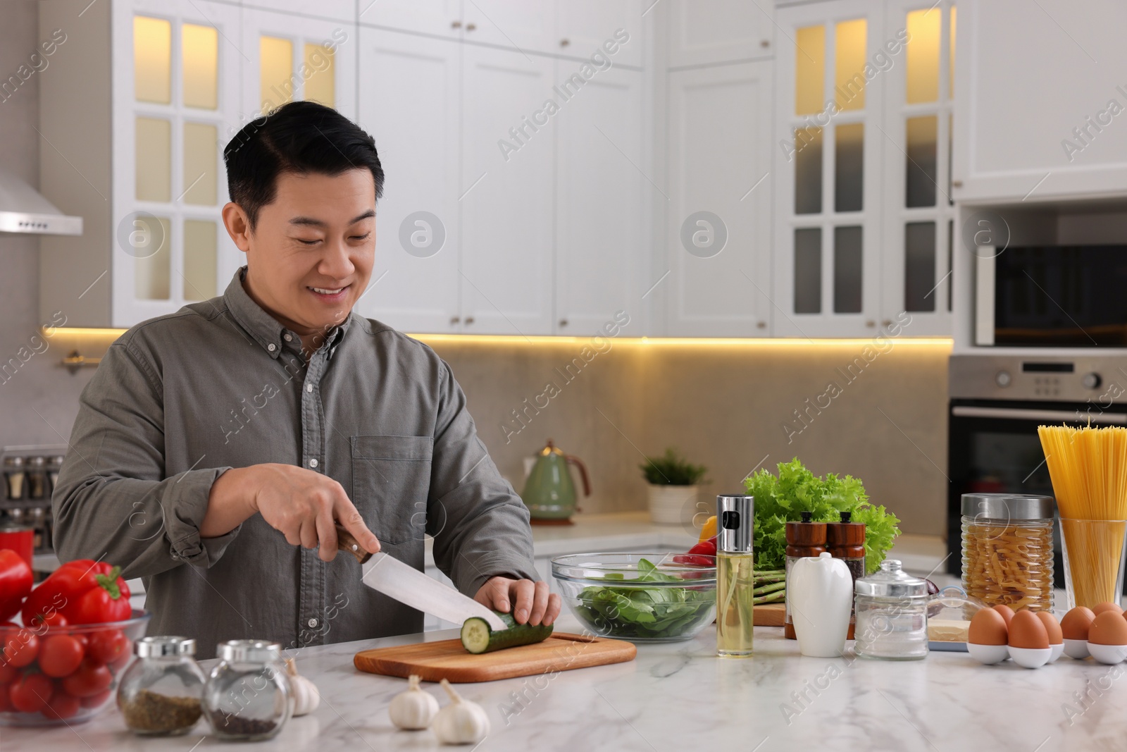 Photo of Cooking process. Man cutting fresh cucumber at countertop in kitchen