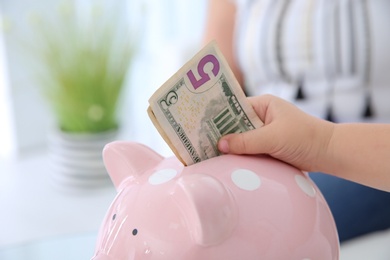 Photo of Little girl putting money into piggy bank, closeup