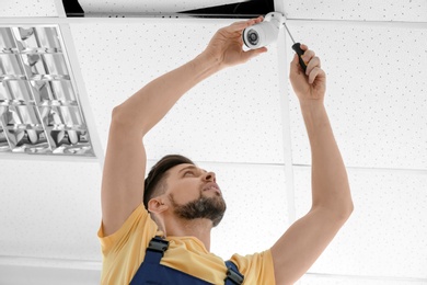 Photo of Technician installing CCTV camera on ceiling indoors