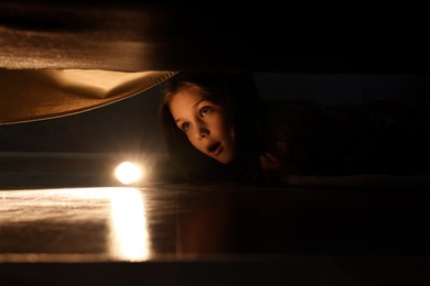 Little girl with flashlight looking for monster under bed at night
