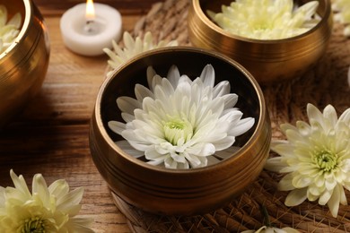 Photo of Tibetan singing bowls, beautiful chrysanthemum flowers and burning candle on wooden table, closeup