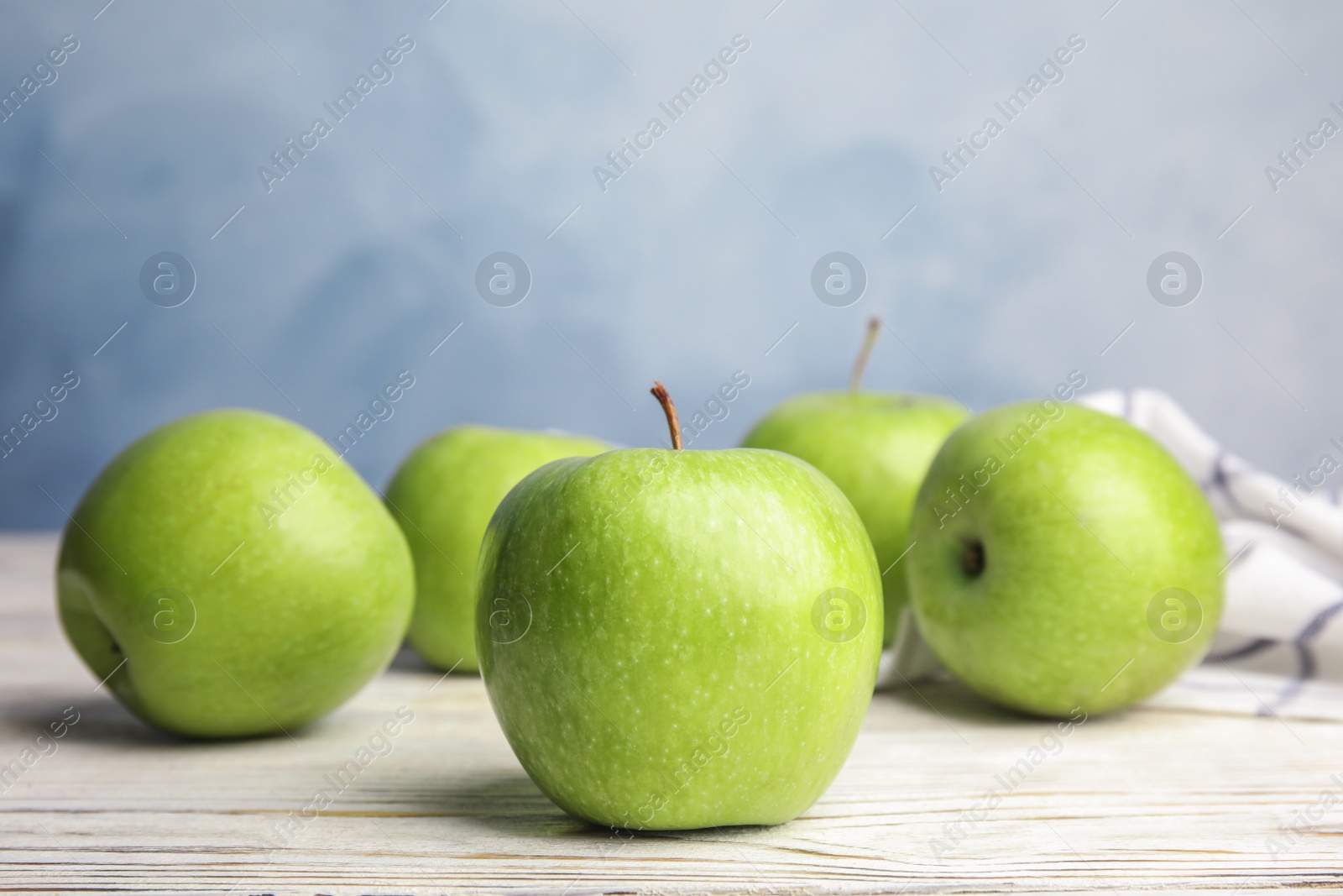 Photo of Fresh ripe green apples on white wooden table against blue background, space for text