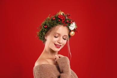Photo of Beautiful young woman wearing Christmas wreath on red background