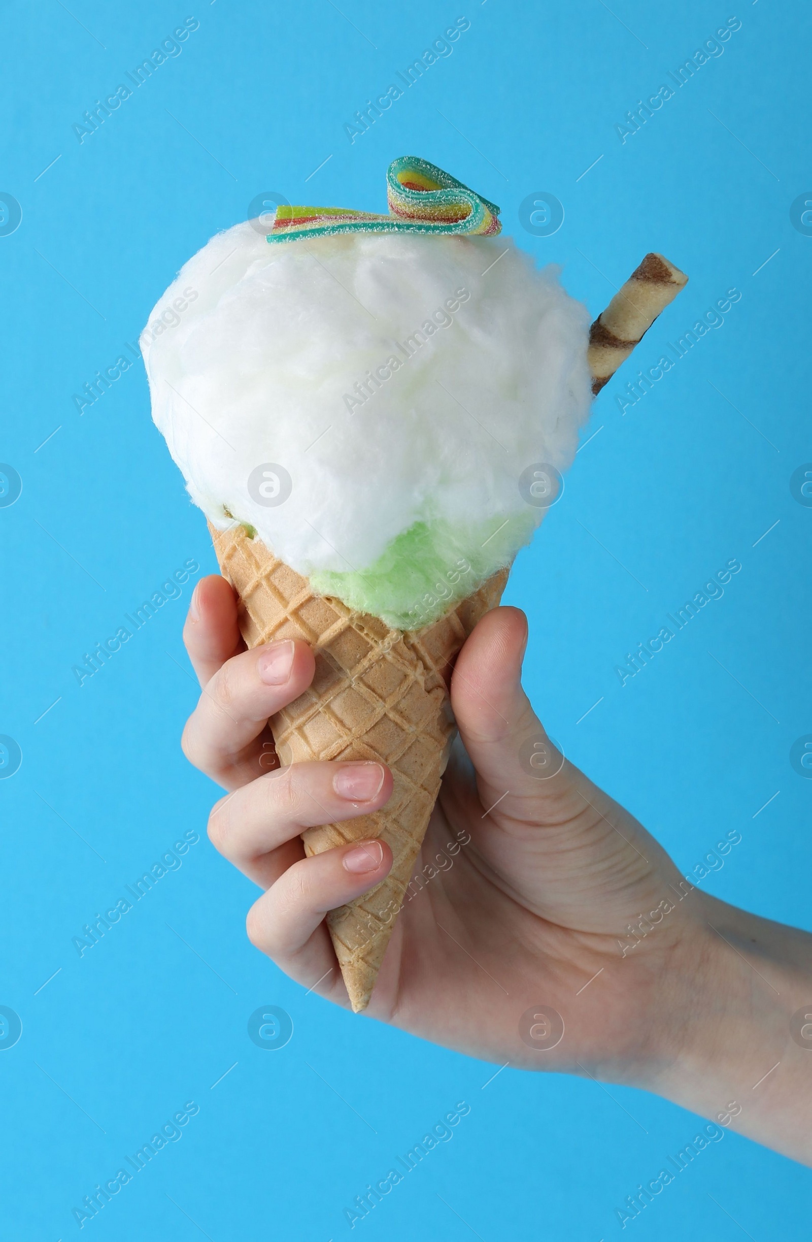 Photo of Woman holding waffle cone with cotton candy on light blue background, closeup