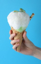 Woman holding waffle cone with cotton candy on light blue background, closeup