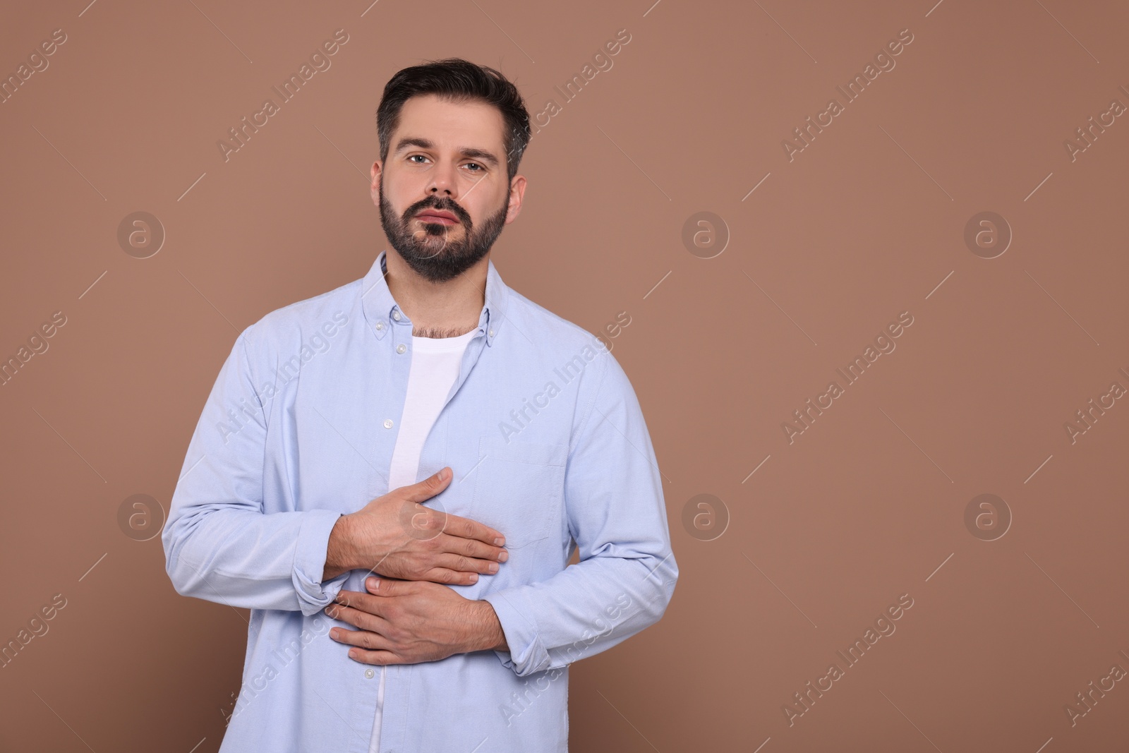 Photo of Man suffering from stomach pain on light brown background, space for text