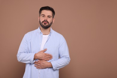 Man suffering from stomach pain on light brown background, space for text