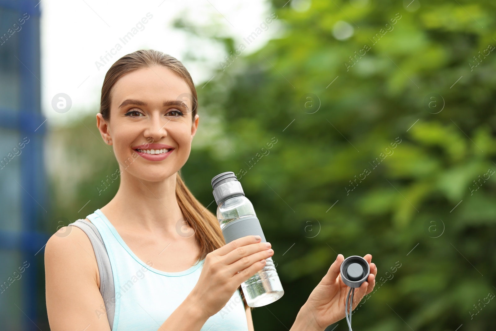 Photo of Young woman with bottle of water outdoors. Refreshing drink