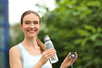 Photo of Young woman with bottle of water outdoors. Refreshing drink