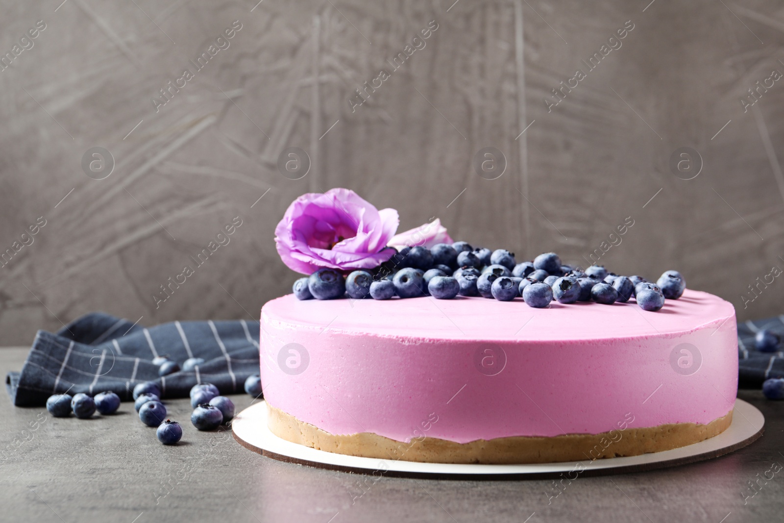 Photo of Tasty blueberry cake decorated with flowers on grey table. Space for text