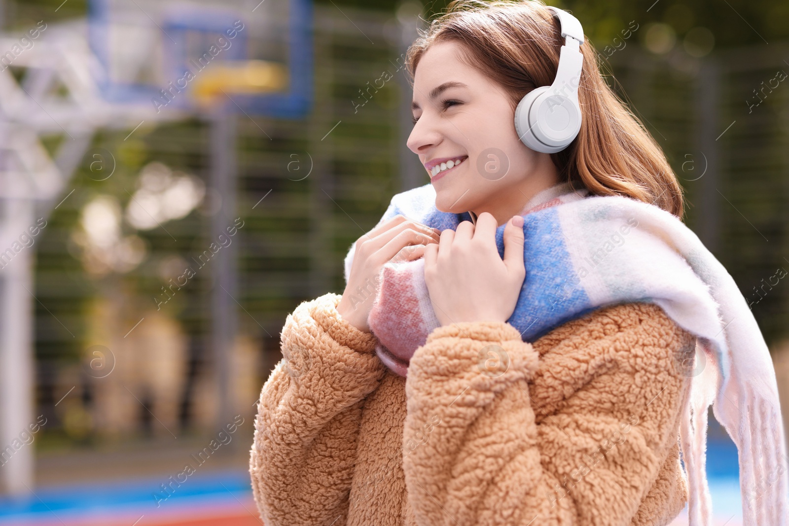 Photo of Beautiful woman in warm scarf listening to music outdoors, space for text