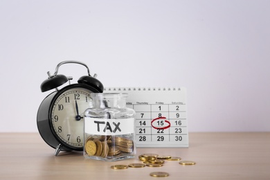 Photo of Glass jar with label "TAX", coins, calendar and alarm clock on table