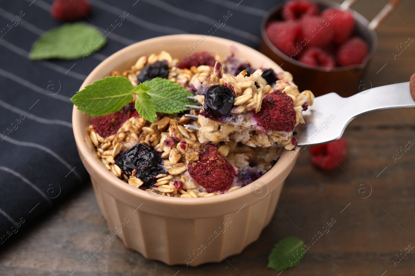 Photo of Eating tasty baked oatmeal with berries at wooden table, closeup