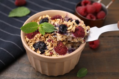 Eating tasty baked oatmeal with berries at wooden table, closeup
