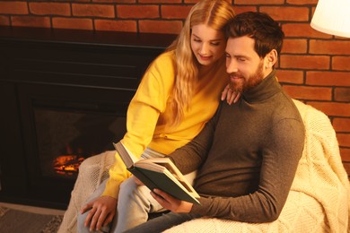 Photo of Lovely couple reading book near fireplace at home