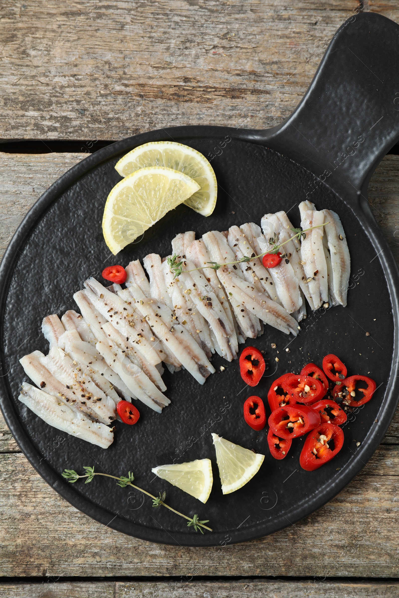 Photo of Tasty anchovies with spices and lemon slices on wooden table, top view