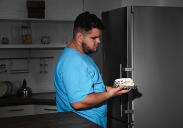 Depressed overweight man taking cake out of refrigerator at night