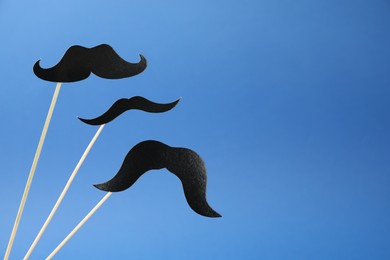 Photo of Fake paper mustaches on sticks against blue background. Space for text