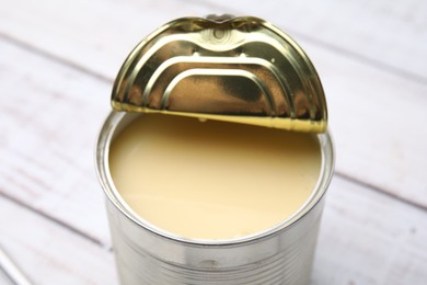 Photo of Tasty condensed milk in tin can on white wooden table, closeup