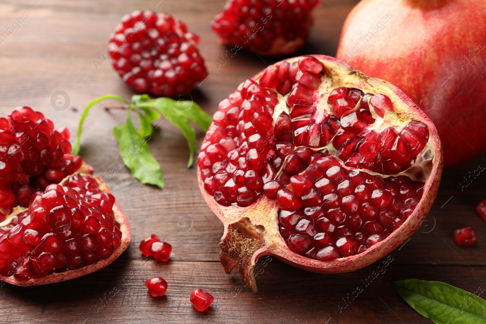 Photo of Cut fresh pomegranate and green leaves on wooden table, closeup