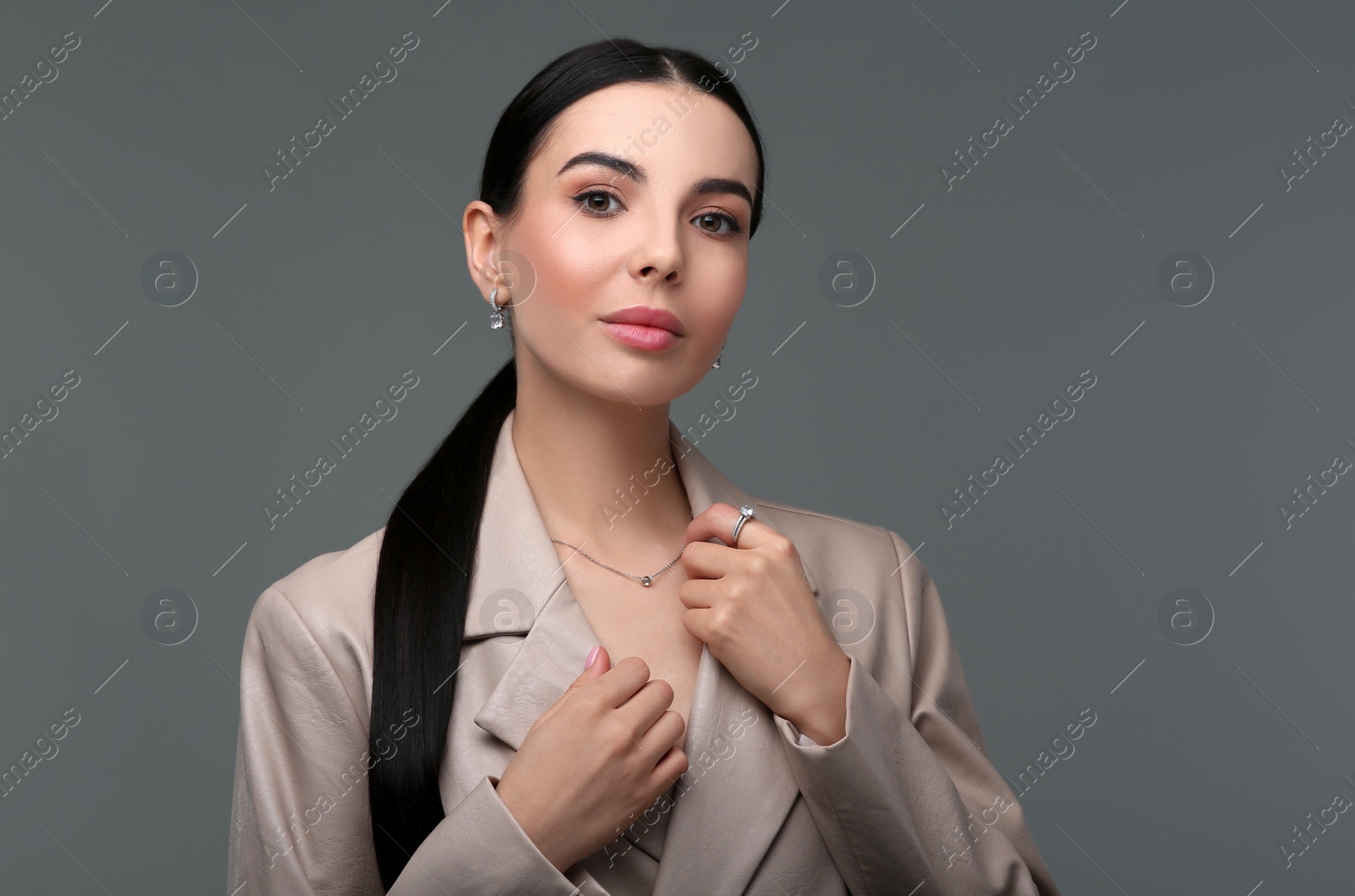 Photo of Beautiful young woman with elegant jewelry on dark grey background