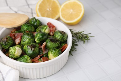 Delicious roasted Brussels sprouts, bacon, lemon and rosemary on white tiled table, closeup. Space for text