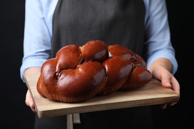 Photo of Closeup view of woman holding homemade braided bread on black background. Traditional Shabbat challah