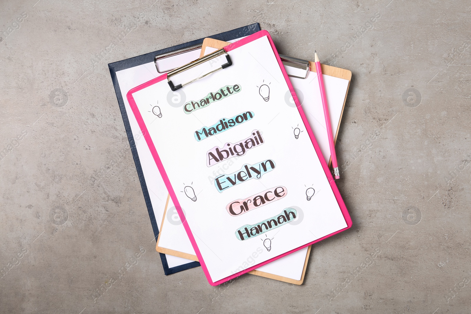 Photo of Clipboards with different baby names and pencil on grey table, top view