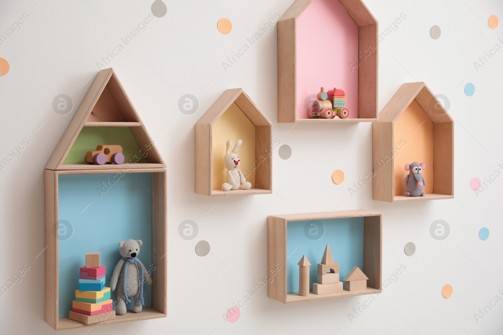 Photo of Stylish house shaped shelves with toys on white wall. Baby room interior design