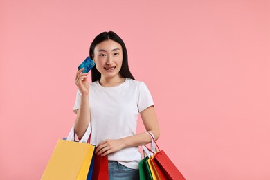 Photo of Smiling woman with shopping bags and credit card on pink background. Space for text