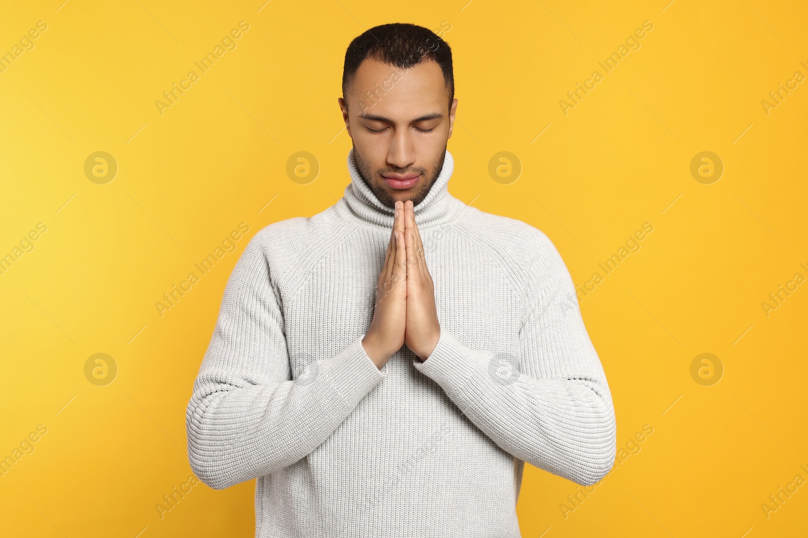 Photo of African American man with clasped hands praying to God on orange background