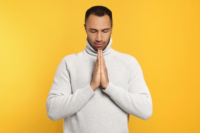 African American man with clasped hands praying to God on orange background