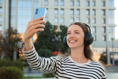 Smiling woman in headphones taking selfie on city street