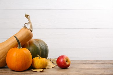 Photo of Happy Thanksgiving day. Many different pumpkins, leaves and apple on wooden table, space for text