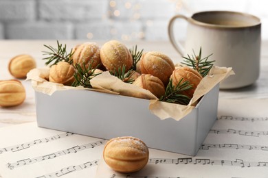 Homemade walnut shaped cookies and fir branches in box on white wooden table, closeup. Bokeh effect