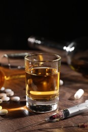 Photo of Alcohol and drug addiction. Whiskey in glass, syringes and pills on wooden table