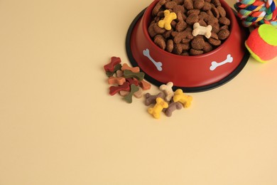 Photo of Dry pet food in bowl, vitamins and toys on beige background, above view. Space for text