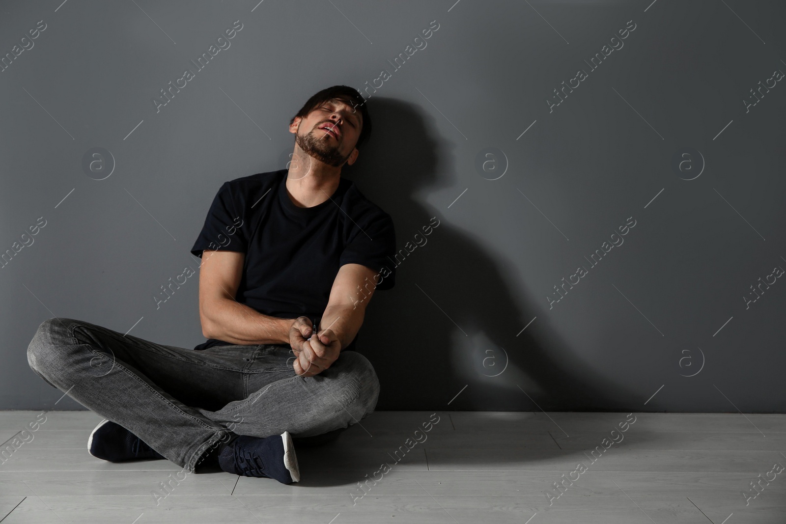 Photo of Male drug addict with syringe sitting near grey wall. Space for text