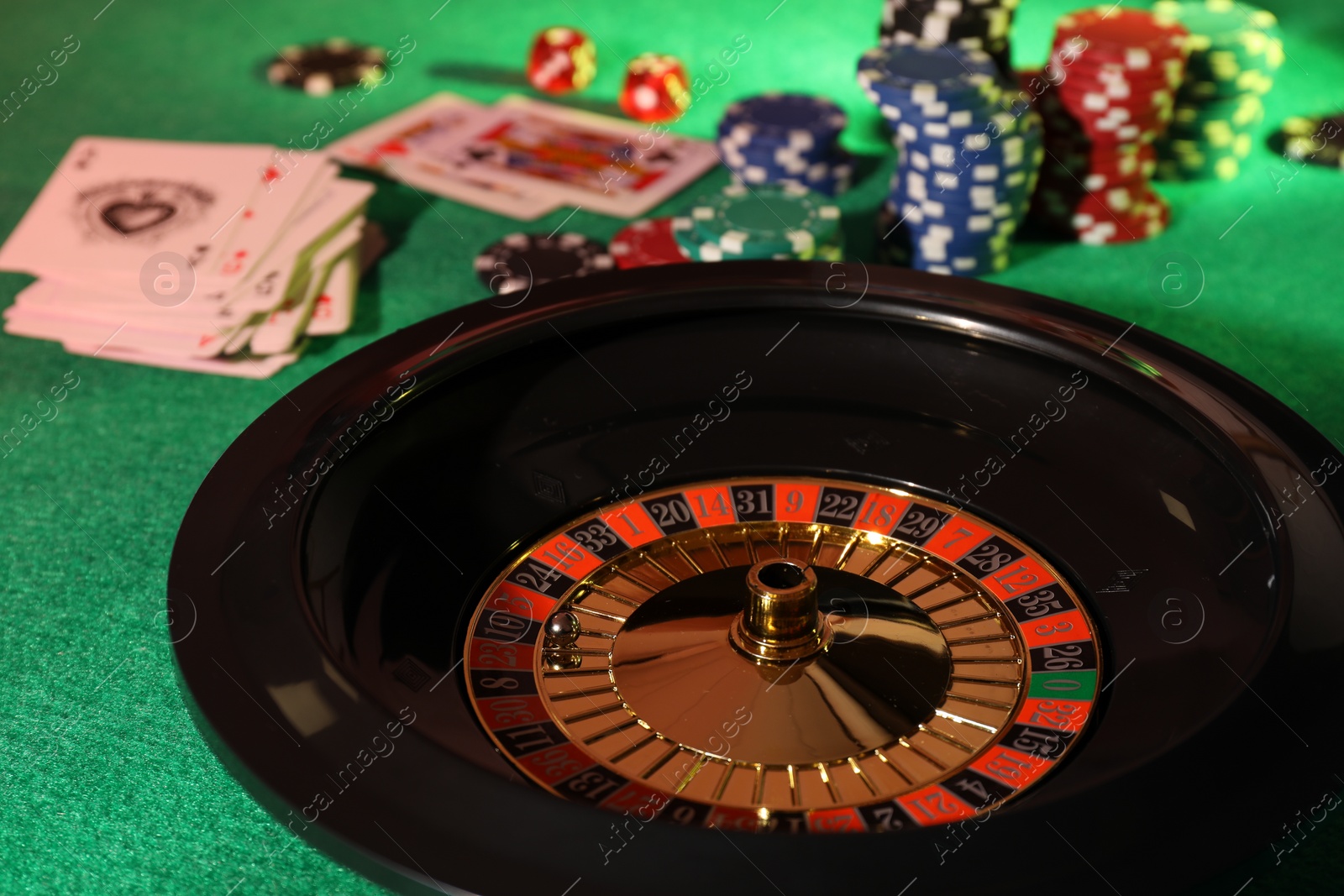 Photo of Roulette wheel with ball, playing cards and chips on green table, closeup. Casino game